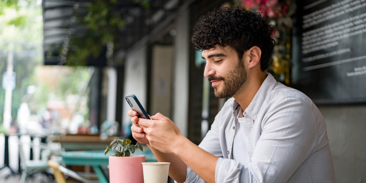 man sitting at outdoor cafe, using cellphone